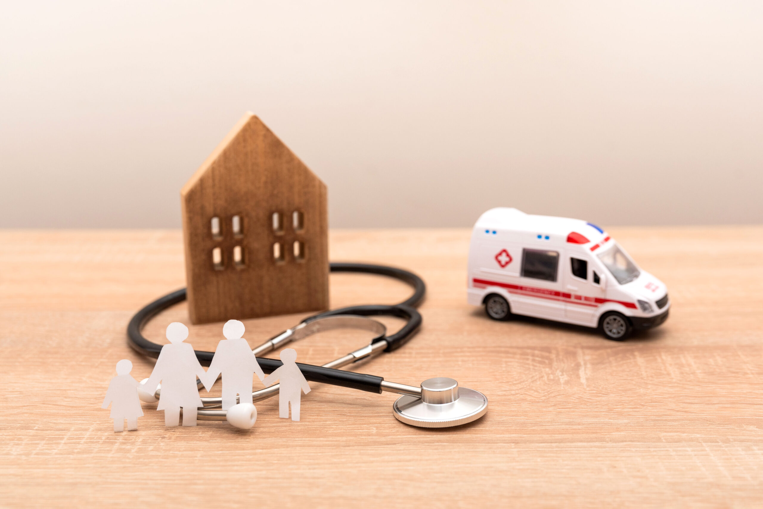 Family healthcare and emergency concept with wooden house, stethoscope and ambulance on wooden desk